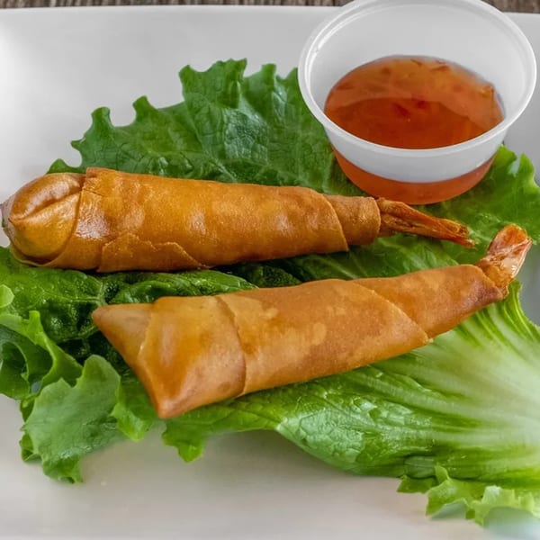 Two golden-brown fried shrimp spring rolls on a bed of lettuce with a side of dipping sauce.