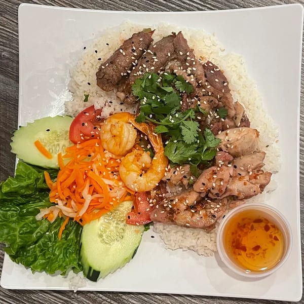 Vietnamese rice plate with grilled beef, chicken, shrimp, fresh vegetables, and dipping sauce.