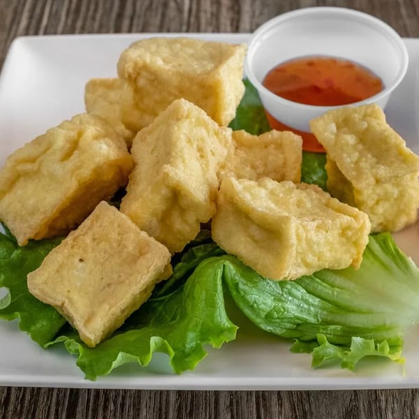Crispy fried tofu pieces on a bed of lettuce with a side of sweet chili dipping sauce.