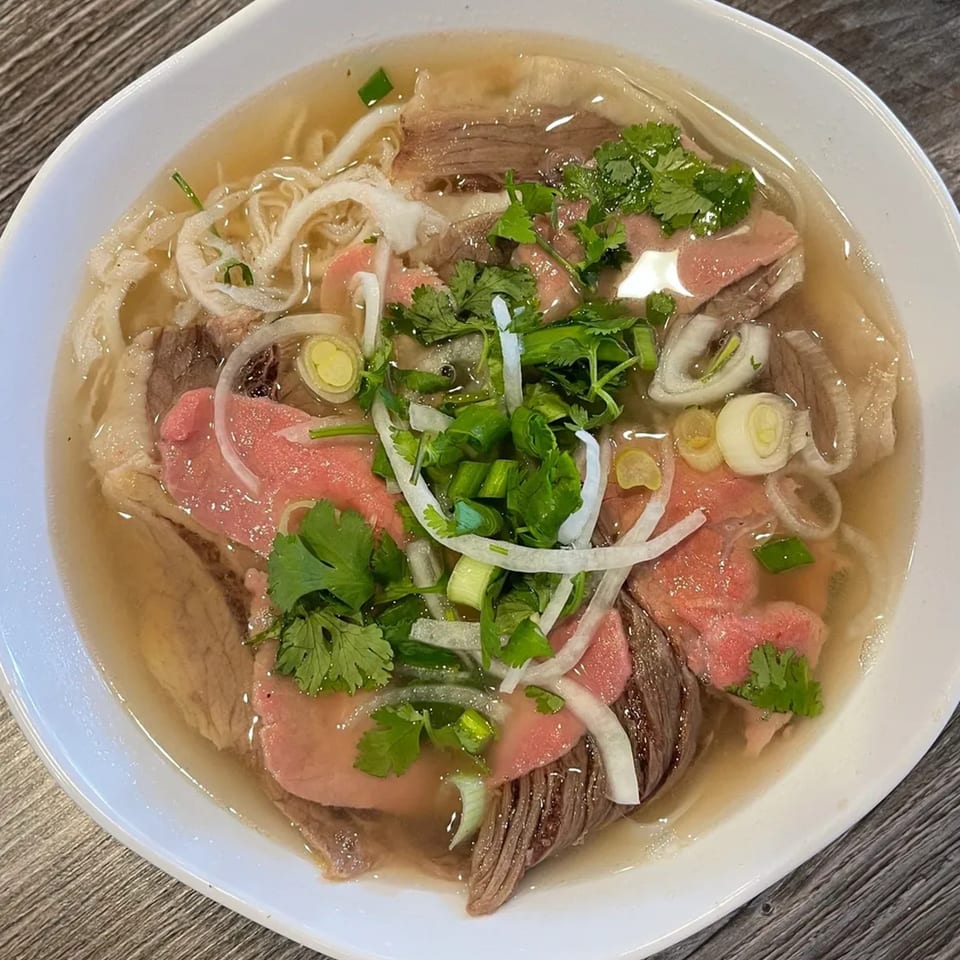 A bowl of Goi Cuon pho with beef, noodles, onions, and cilantro in a clear broth.